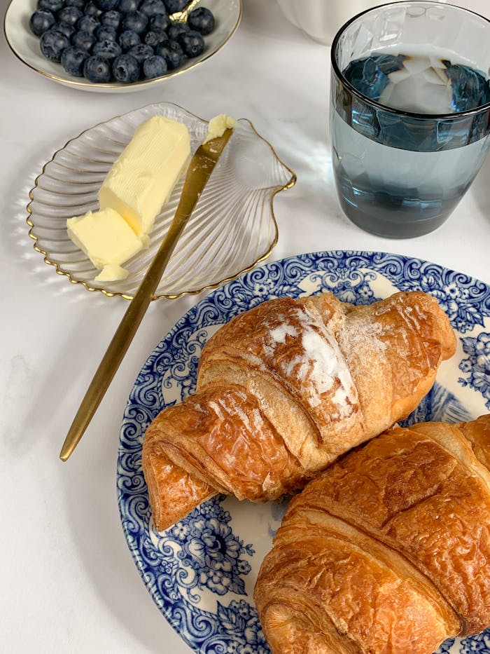 Elegant breakfast setting featuring croissants, butter, blueberries, and a glass of water.
